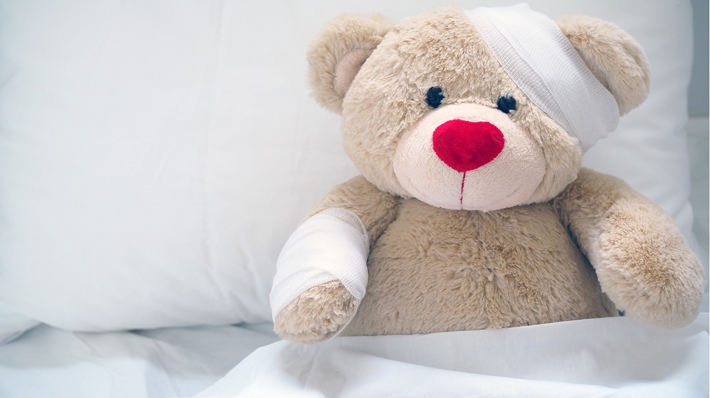 Erste Hilfe bei Kindern: Ein Teddybär ist im Bett und hat einen Verband um seinen Kopf.